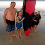 Family stands with surfboard on the beach to take picture