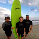 three people pose with green surfboard on the beach