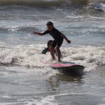 little boy surfing a wave with instructor helping behind