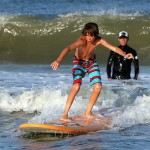 boy in striped bathing suit surfs a wave on orange surfboard