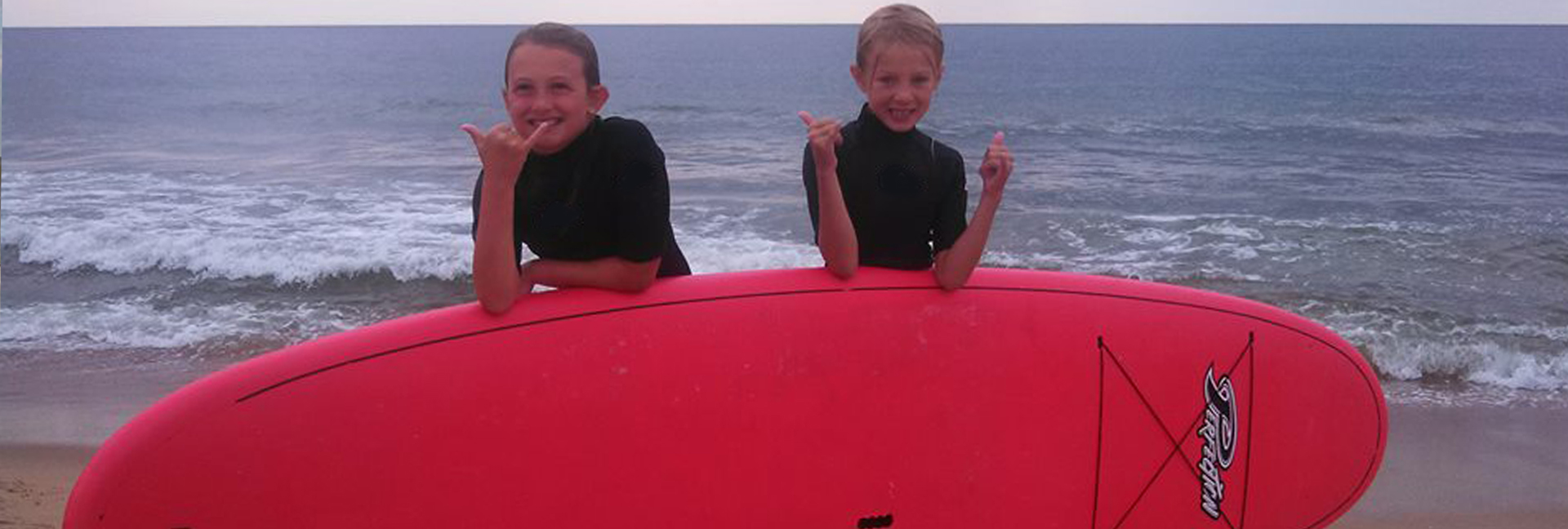 boy and girl pose behind a red surboard with a thumbs up