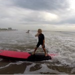 little boy waving to camera as he surfs