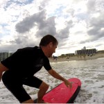 Guy wearing ear plugs surfs into the shallow water
