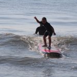 Young boy standing on surfboard with instructor behind him