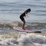 Girl surfing in wetsuit on red and black surfboard